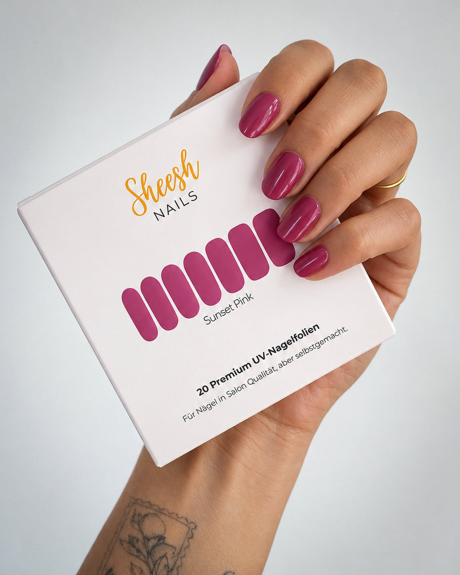 Hand mit glänzenden Nägeln in Beerenpink hält die Sunset Pink Verpackung von SHEESH Nails mit 20 UV-Nagelfolien.
