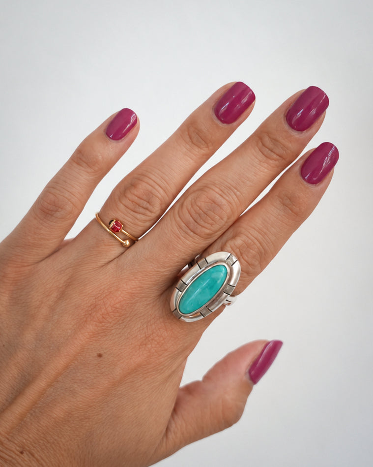 Hand mit goldenen und silbernen Ringen und glänzenden Sunset Pink UV-Nagelfolien in Beerenpink.
