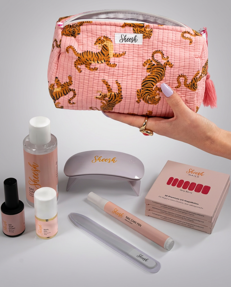 Sheesh Nails Starterset mit rosa Kosmetiktasche mit Tigerprint, UV-Lampe, UV Top Coat, Nail Oil, Nail Care Pen, Glasfeile, Nail Cleaner und drei Packungen UV-Nagelfolien auf weißem Hintergrund