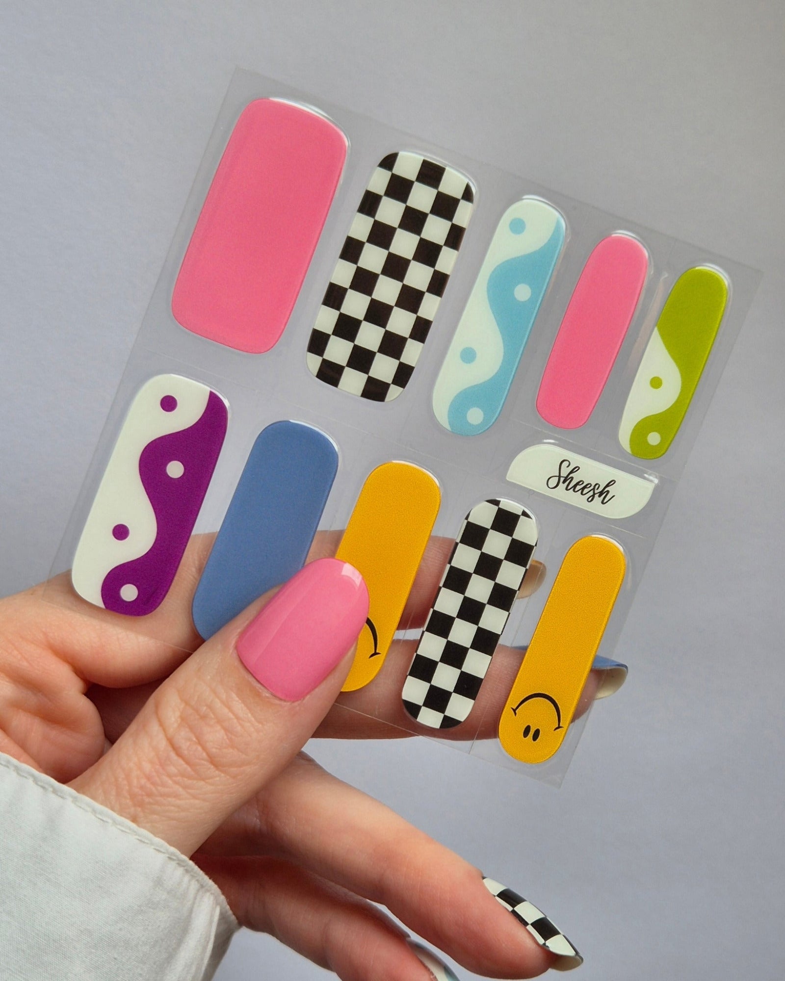 Sheesh Nails – Tip Tok – bunte Nagelfolien im Retro-Design mit fröhlichen Smileys, Karomuster und sanften Blautönen. Perfekte Passform und starker Halt für kreative, verspielte Maniküren im Trendstil der 2000er.
