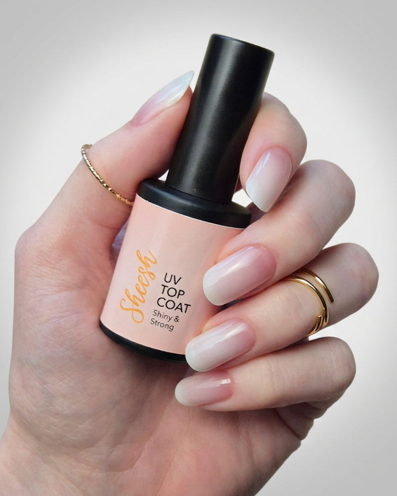 SHEESH Nails UV Top Coat wird in einer Hand mit glänzender milchig-rosa Maniküre vor hellem Studiohintergrund gehalten