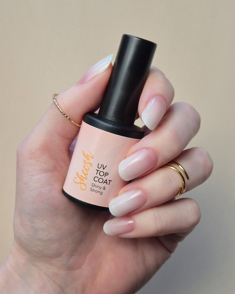 SHEESH Nails UV Top Coat wird in einer Hand mit glänzender milchig-rosa Maniküre vor hellem Studiohintergrund gehalten