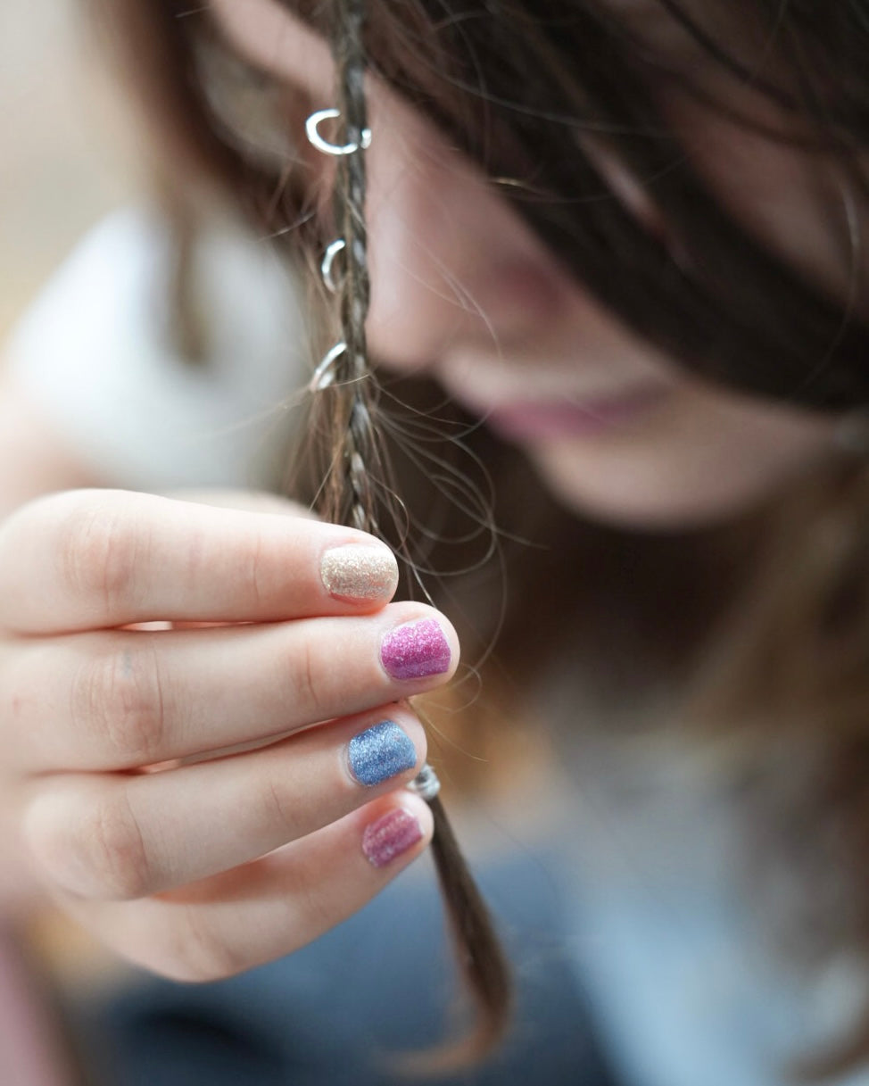 Sheesh Kindernagelfolie Twinkle. Kinderhand mit Nagelfolie hält Haarsträhne mit Silberringen im Haar. 
