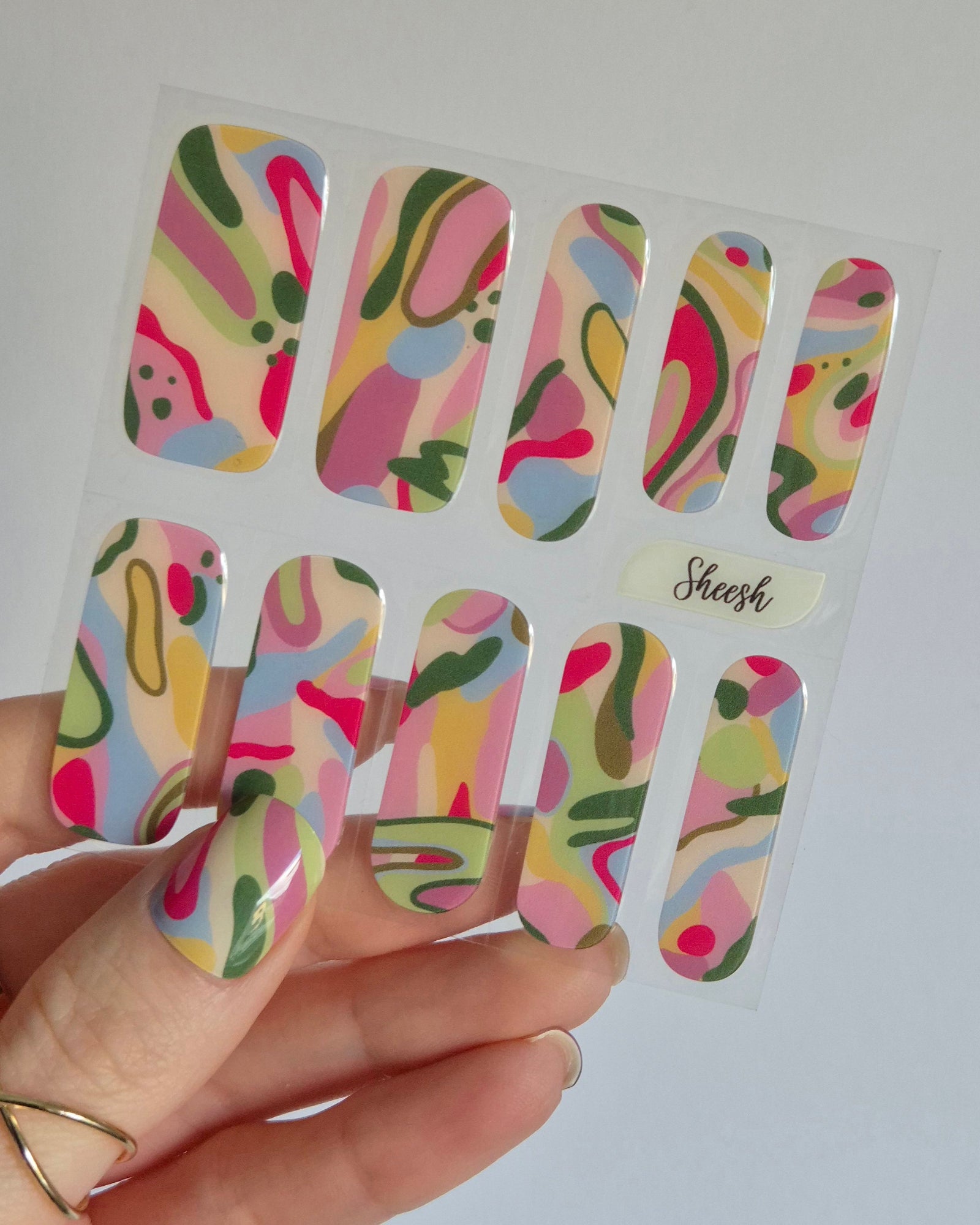 SHEESH Nagelfolie Arty, entworfen in Kooperation mit der abstrakten Künstlerin Robyn Cher Klittich. Die Nägel zeigen ein farbenfrohes, künstlerisches Design in Rosa-, Gelb-, Grün- und Blautönen. Inspiriert von moderner Malerei vereint Arty Farbe, Emotion und Kreativität – eine Limited Edition für alle, die Nail Art lieben.