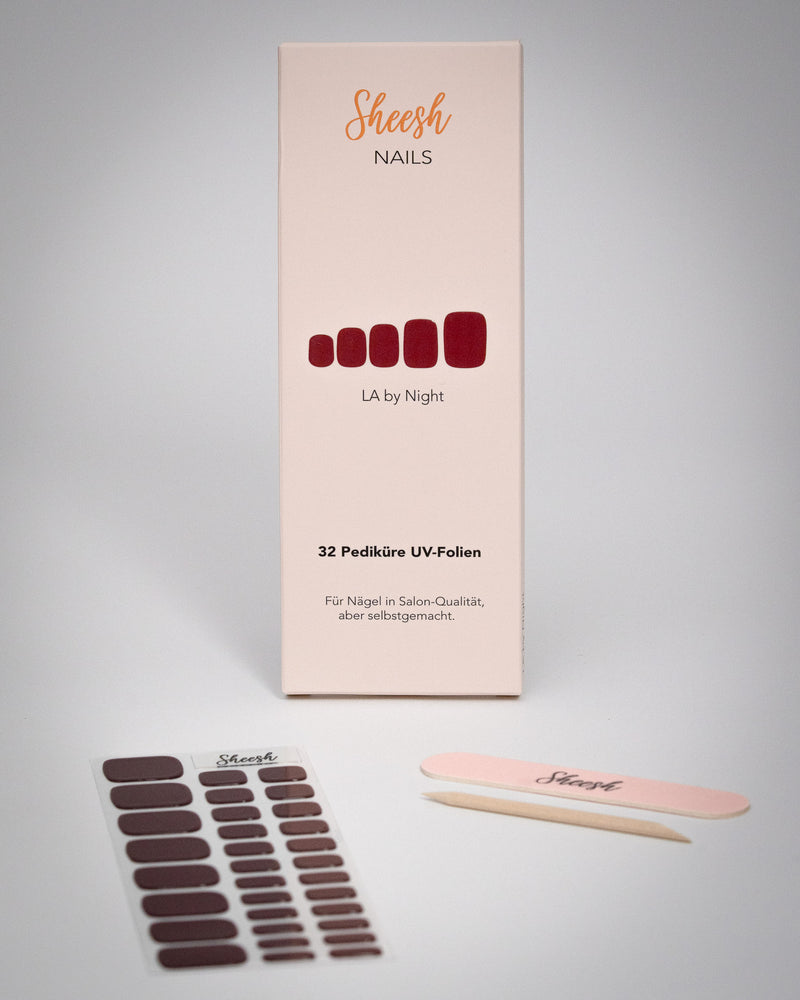 Sheesh Nails Pediküre UV-Folien „LA by Night“ in elegantem Dunkelrot. Verpackung mit 32 UV-Folien, Nagelfeile und Holzstäbchen auf weißem Hintergrund. Für eine langanhaltende Pediküre in Salon-Qualität – einfach mit UV-Licht 