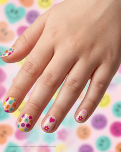 SHEESH Nails – Big Smile, Bild 03: Kinderhand mit bunten Big Smile Nagelfolien vor rosa Hintergrund mit Smileys und Blumen.