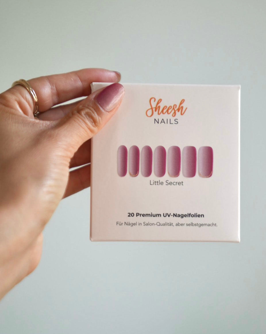 SHEESH Nails – Little Secret – UV-Nagelfolien in Rosa-Ombre mit Goldrand, Bild 05: Hand hält die Verpackung der UV-Nagelfolie „Little Secret“.