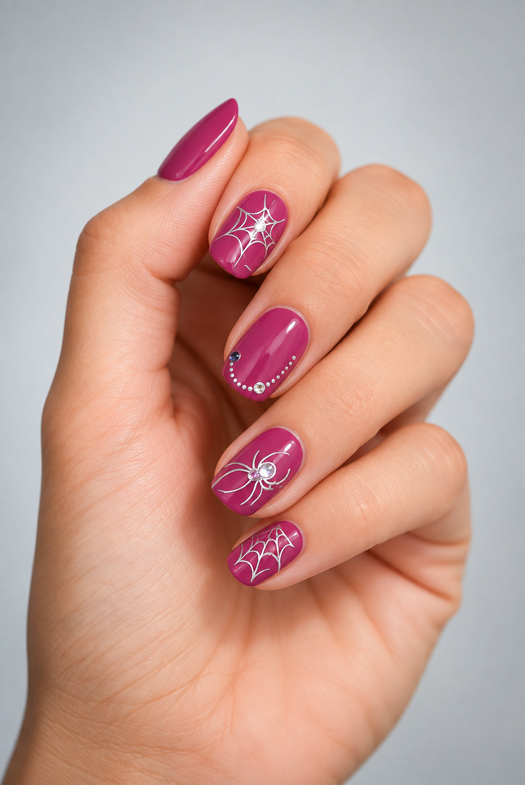 SHEESH Nails – Nail Sticker Halloween, Bild 01: auf beerfarbener Maniküre mit silbernen Spinnen- und Spinnennetzmotiven sowie Strasssteinen.