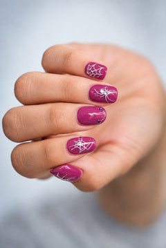 SHEESH Nails – Nail Sticker Halloween, Bild 03: Nahaufnahme einer Halloween-Maniküre mit silbernen Spinnen- und Spinnennetzstickern auf beerfarbenen Nägeln.