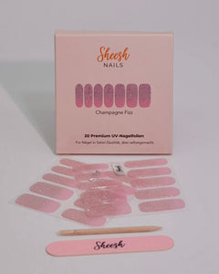 Produktaufnahme der Sheesh Nails UV-Nagelfolie „Champagne Fizz“. Die Folien zeigen ein funkelndes Rosé-Pink mit feinem Glitzerfinish, das einen luxuriösen, festlichen Look erzeugt. Die edle Verpackung und das beigelegte Zubehör unterstreichen die hochwertige Qualität – ideal für elegante Anlässe oder glamouröse Alltagsmomente.