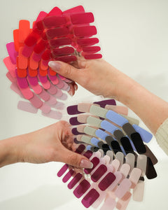 Produktfoto eines Folienfächers mit verschiedenen Sheesh Nails UV-Nagelfolien in zahlreichen Farben. Die Hand hält den aufgefächerten Überblick von Rot-, Rosa-, Lila- und Blautönen. Ideal zur Farbauswahl und Präsentation des Sortiments – professionell, übersichtlich und ästhetisch arrangiert.