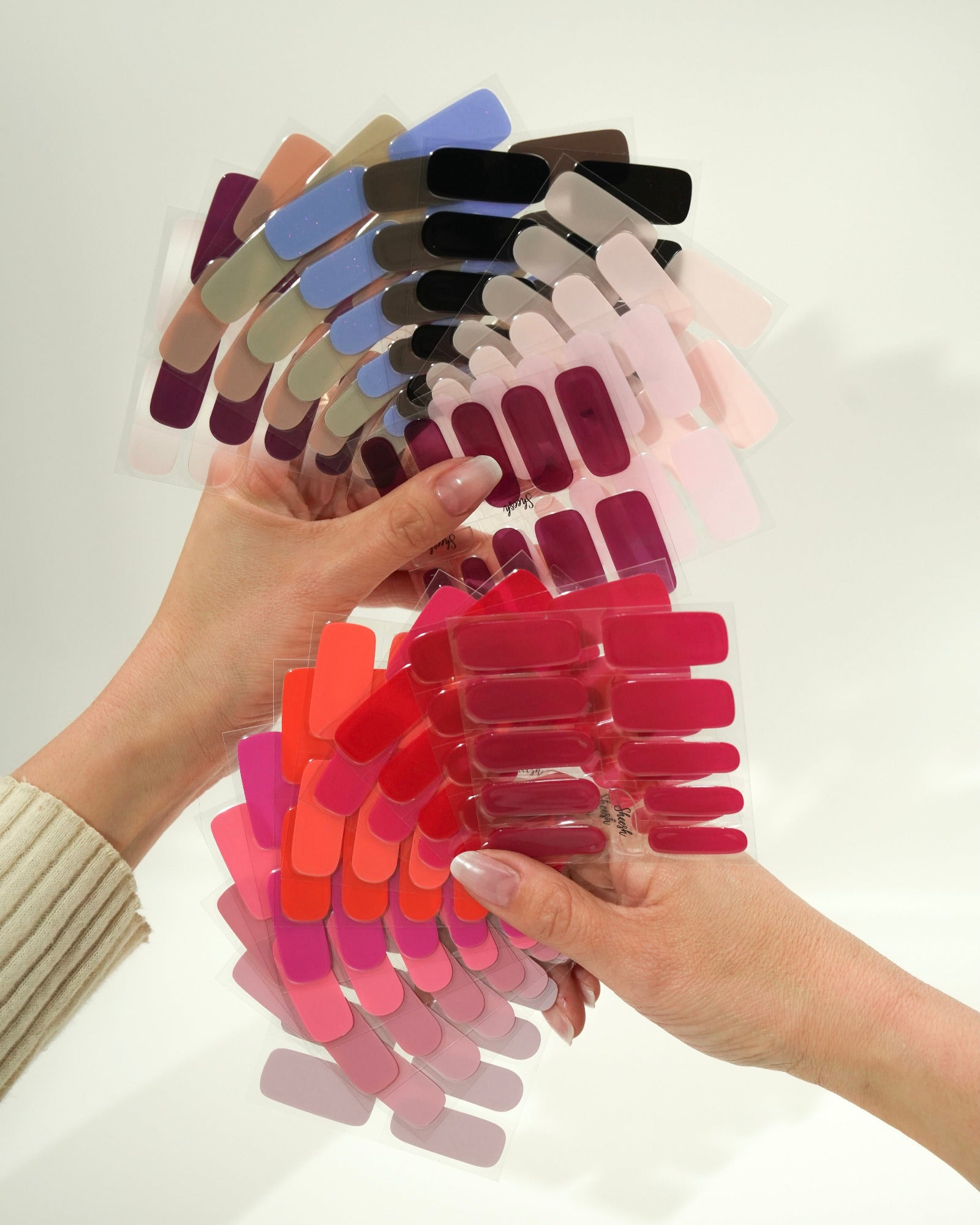 Produktfoto eines Folienfächers mit verschiedenen Sheesh Nails UV-Nagelfolien in zahlreichen Farben. Die Hand hält den aufgefächerten Überblick von Rot-, Rosa-, Lila- und Blautönen. Ideal zur Farbauswahl und Präsentation des Sortiments – professionell, übersichtlich und ästhetisch arrangiert.