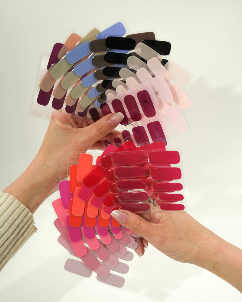 Produktfoto eines Folienfächers mit verschiedenen Sheesh Nails UV-Nagelfolien in zahlreichen Farben. Die Hand hält den aufgefächerten Überblick von Rot-, Rosa-, Lila- und Blautönen. Ideal zur Farbauswahl und Präsentation des Sortiments – professionell, übersichtlich und ästhetisch arrangiert.