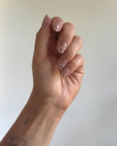 Hand trägt die Sheesh Nails UV-Nagelfolie Half Life. Die Folien zeigen ein transparentes Design mit feinem Leopardenmuster in Braun- und Beigetönen auf zartem Nude-Hintergrund. Der Look wirkt elegant, modern und leicht verspielt – perfekt für trendige Animal-Print-Maniküren mit stilvollem Finish.