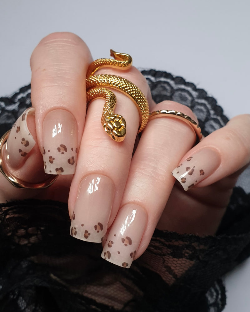 Hand trägt die Sheesh Nails UV-Nagelfolie Half Life. Die Folien zeigen ein transparentes Design mit feinem Leopardenmuster in Braun- und Beigetönen auf zartem Nude-Hintergrund. Der Look wirkt elegant, modern und leicht verspielt – perfekt für trendige Animal-Print-Maniküren mit stilvollem Finish.