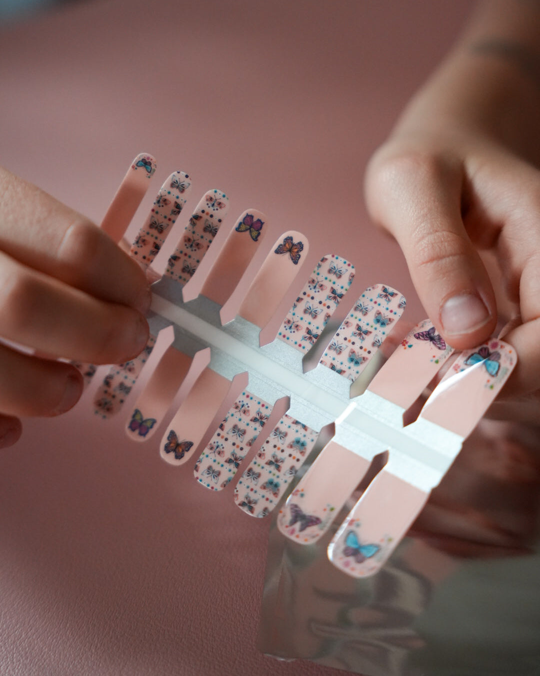 Nahaufnahme einer Kinderhand mit den Sheesh Nails Kinder-Nagelfolien „Butterfly“. Die selbstklebenden Sticker zeigen ein verspieltes Design mit bunten Schmetterlingen und Blüten auf rosafarbenem Grund. Das deckende Finish sorgt für einen fröhlichen, kindgerechten Look. Hautfreundlich, ungiftig und leicht anzubringen – ideal für kreative Kinder-Maniküren mit Farbe und Fantasie.