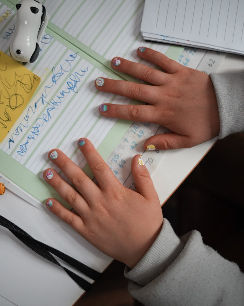 Nahaufnahme einer Kinderhand mit den Sheesh Nails Kinder-Nagelfolien „Einhorn“. Die selbstklebenden Sticker zeigen fröhliche Einhorn-Motive auf pastellfarbenem Hintergrund mit Regenbögen und Sternen. Das deckende Finish sorgt für einen bunten, verspielten Look. Hautfreundlich, ungiftig und leicht aufzubringen – ideal für kreative Kinder-Maniküren mit Magie und Fantasie.
