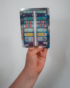 Nahaufnahme einer Kinderhand, die die Sheesh Nails Kinder-Nagelfolien „Einhorn“ in der Verpackung hält. Die selbstklebenden Sticker zeigen bunte Einhorn-Motive, Regenbögen und Sterne in zarten Pastelltönen. Das deckende Finish sorgt für einen fröhlichen, kindgerechten Look. Hautfreundlich, ungiftig und leicht anzubringen – ideal für kreative Kinder-Maniküren voller Fantasie und Farbe.