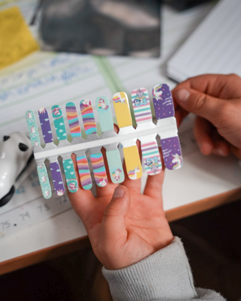 Nahaufnahme einer Kinderhand mit den Sheesh Nails Kinder-Nagelfolien „Einhorn“. Die selbstklebenden Sticker zeigen ein verspieltes Design mit Einhörnern, Regenbögen und glitzernden Details in Pastellfarben. Das deckende Finish sorgt für einen farbenfrohen, magischen Look. Hautfreundlich, ungiftig und einfach anzubringen – ideal für kreative Kinder-Maniküren mit Fantasie und Spaß.