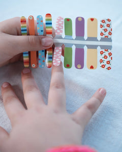 Nahaufnahme einer Kinderhand mit den Sheesh Nails Kinder-Nagelfolien „Happy“. Die bunten, selbstklebenden Sticker zeigen fröhliche Muster in Regenbogenfarben, Herzen und Punkten – perfekt für kleine Nail-Artists, die Spaß an Farbe und Kreativität haben. Die Sticker sind deckend, leicht aufzubringen und rückstandsfrei wieder zu entfernen – ganz ohne UV-Lampe. Hautfreundlich, ungiftig und ideal für kreative Kinder-Maniküren voller Freude und Fantasie.