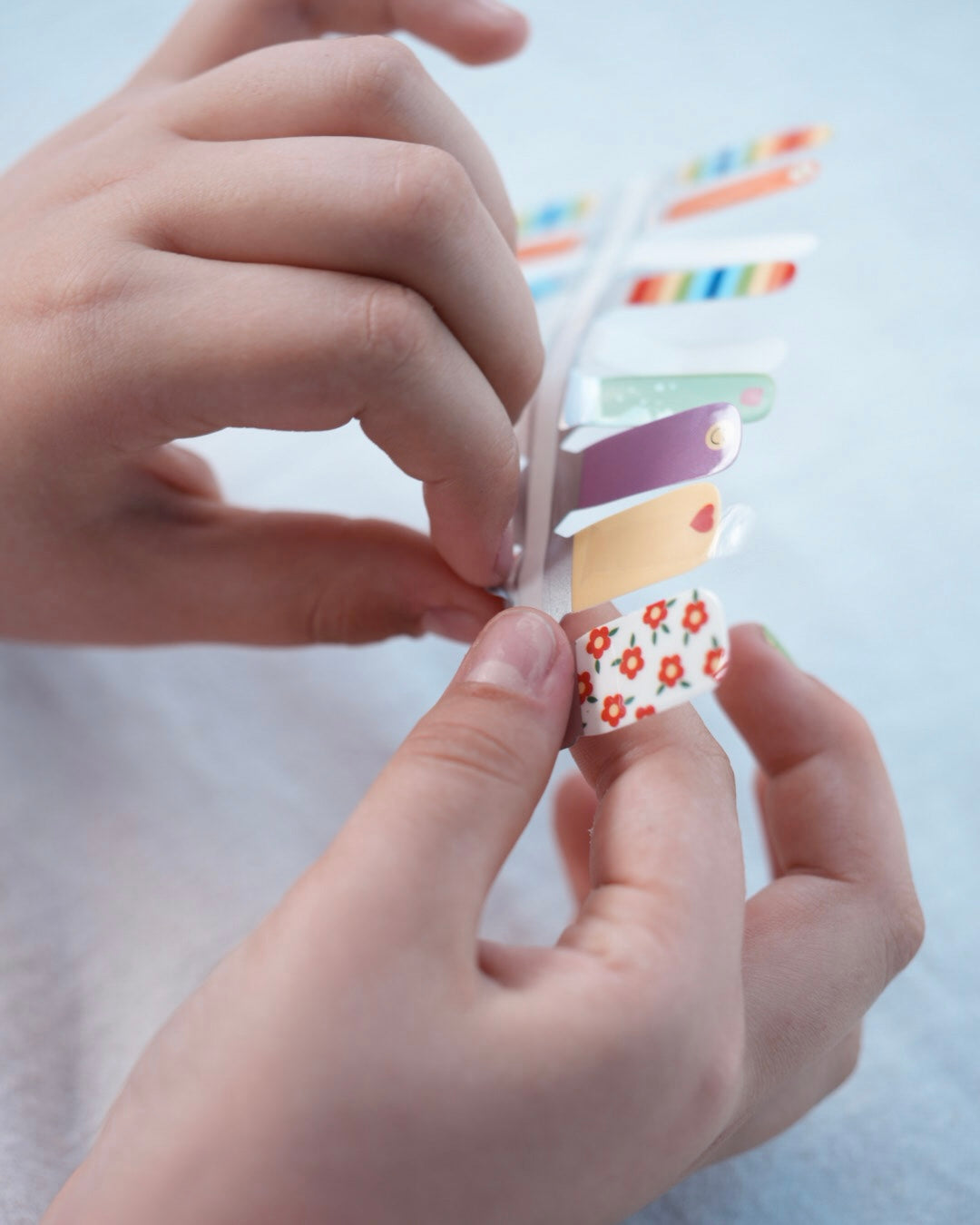 Nahaufnahme einer Kinderhand mit den Sheesh Nails Kinder-Nagelfolien „Happy“. Die bunten, selbstklebenden Sticker zeigen fröhliche Muster in Regenbogenfarben, Herzen und Punkten – perfekt für kleine Nail-Artists, die Spaß an Farbe und Kreativität haben. Die Sticker sind deckend, leicht aufzubringen und rückstandsfrei wieder zu entfernen – ganz ohne UV-Lampe. Hautfreundlich, ungiftig und ideal für kreative Kinder-Maniküren voller Freude und Fantasie.