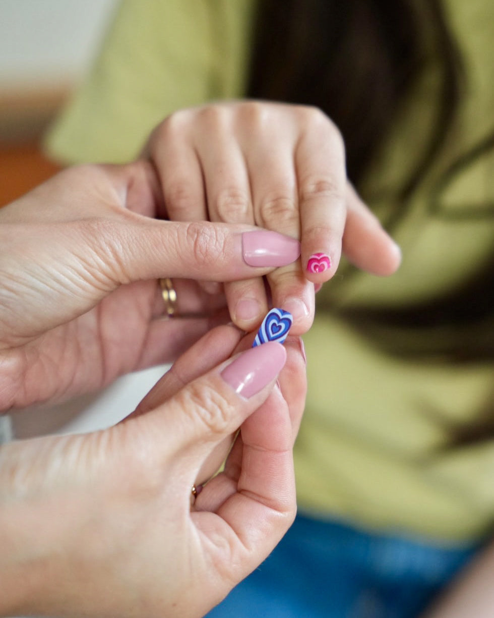 Nahaufnahme eines Kindes mit Sheesh Nails Kinder-Nagelfolien „Herzi“. Die selbstklebenden Sticker zeigen bunte Herzmotive auf farbenfrohem Hintergrund. Das Design wirkt verspielt und kindgerecht. Die Folien sind hautfreundlich, ungiftig und leicht anzubringen – ideal für kreative Kinder-Maniküren mit Liebe zum Detail.