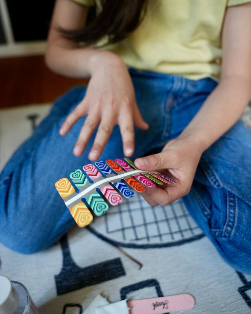 Nahaufnahme eines Kindes mit Sheesh Nails Kinder-Nagelfolien „Herzi“. Die selbstklebenden Sticker zeigen bunte Herzmotive auf farbenfrohem Hintergrund. Das Design wirkt verspielt und kindgerecht. Die Folien sind hautfreundlich, ungiftig und leicht anzubringen – ideal für kreative Kinder-Maniküren mit Liebe zum Detail.