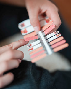 Nahaufnahme einer Kinderhand, die Sheesh Nails Kinder-Nagelfolien „Hot Dog“ aufträgt. Die selbstklebenden Sticker zeigen ein fröhliches Design in Orange mit Streifen und kleinen Hundemotiven. Das deckende Finish sorgt für einen lebendigen, kindgerechten Look. Hautfreundlich, ungiftig und leicht anzubringen – ideal für kreative Kinder-Maniküren mit Spaß und Farbe.