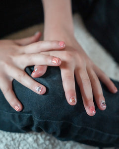 Nahaufnahme einer Kinderhand, die Sheesh Nails Kinder-Nagelfolien „Hot Dog“ aufträgt. Die selbstklebenden Sticker zeigen ein fröhliches Design in Orange mit Streifen und kleinen Hundemotiven. Das deckende Finish sorgt für einen lebendigen, kindgerechten Look. Hautfreundlich, ungiftig und leicht anzubringen – ideal für kreative Kinder-Maniküren mit Spaß und Farbe.