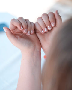 Nahaufnahme einer Kinderhand mit den Sheesh Nails Kinder-Nagelfolien „Lilly“. Die transparenten Sticker zeigen feine, weiße Blumen und lassen die natürliche Nagelfarbe sanft durchscheinen. Ideal für kleine Nail-Artists, die verspielte, zarte Designs lieben. Die selbstklebenden Folien sind leicht anzubringen, hautfreundlich, ungiftig und lassen sich rückstandsfrei wieder entfernen – ganz ohne UV-Lampe. Perfekt für kreative Kinder-Maniküren mit einem natürlichen und liebevollen Look.