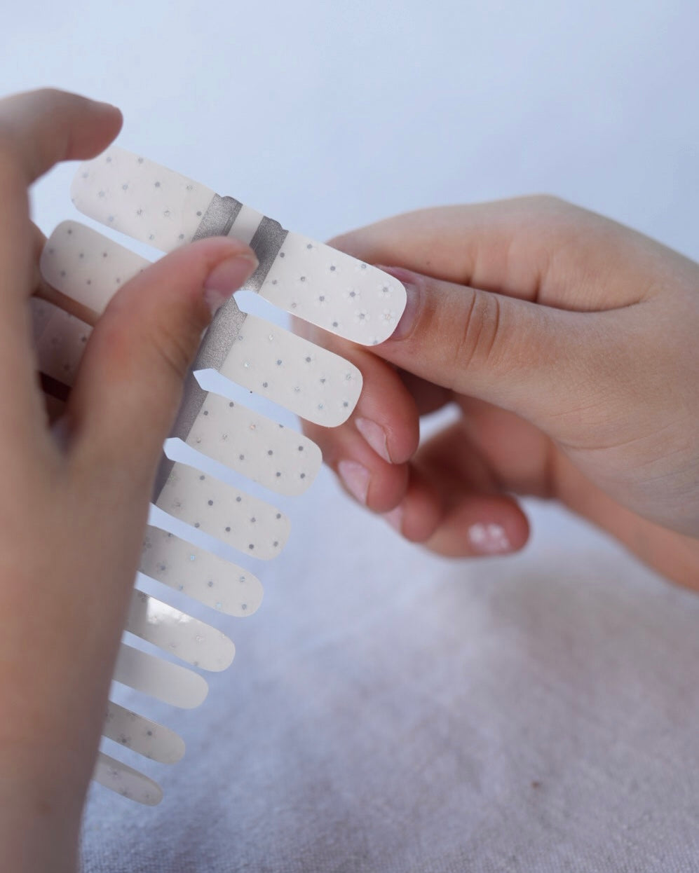 Nahaufnahme einer Kinderhand mit den Sheesh Nails Kinder-Nagelfolien „Lilly“. Die transparenten Sticker zeigen feine, weiße Blumen und lassen die natürliche Nagelfarbe sanft durchscheinen. Ideal für kleine Nail-Artists, die verspielte, zarte Designs lieben. Die selbstklebenden Folien sind leicht anzubringen, hautfreundlich, ungiftig und lassen sich rückstandsfrei wieder entfernen – ganz ohne UV-Lampe. Perfekt für kreative Kinder-Maniküren mit einem natürlichen und liebevollen Look.