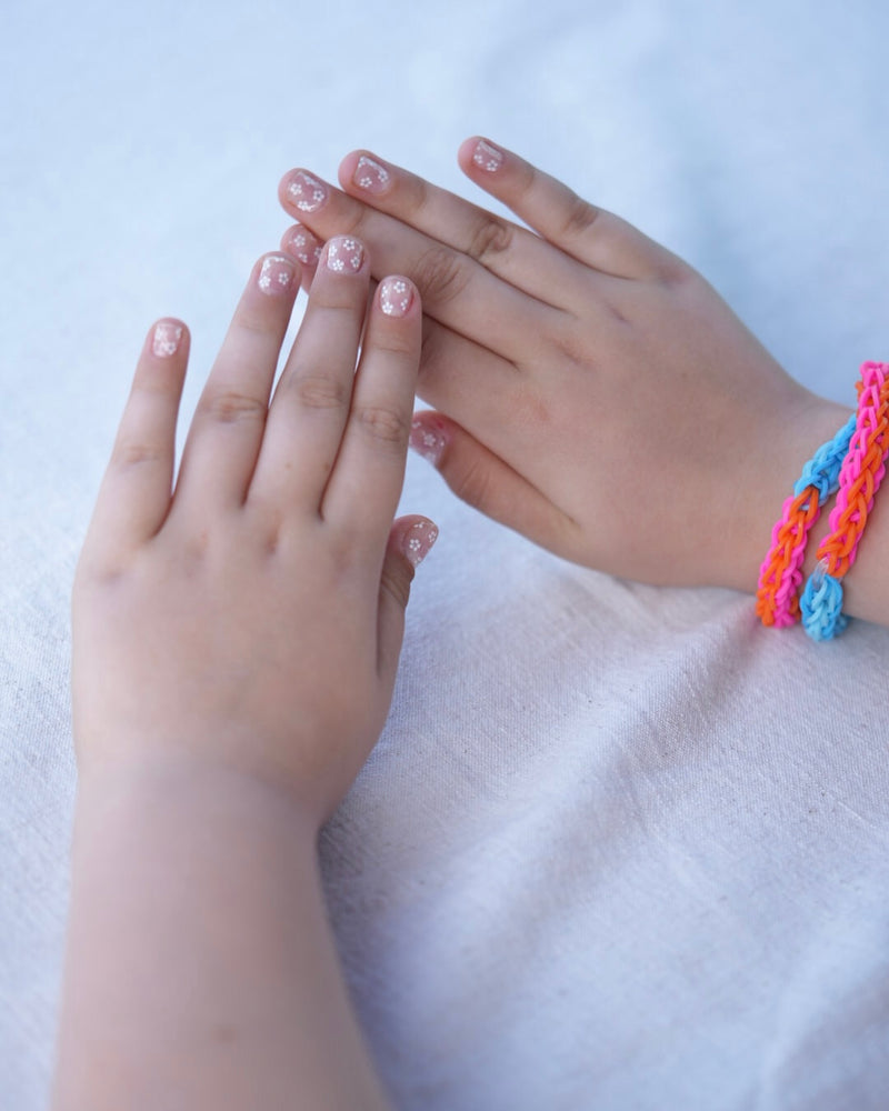 Nahaufnahme einer Kinderhand mit den Sheesh Nails Kinder-Nagelfolien „Lilly“. Die transparenten Sticker zeigen feine, weiße Blumen und lassen die natürliche Nagelfarbe sanft durchscheinen. Ideal für kleine Nail-Artists, die verspielte, zarte Designs lieben. Die selbstklebenden Folien sind leicht anzubringen, hautfreundlich, ungiftig und lassen sich rückstandsfrei wieder entfernen – ganz ohne UV-Lampe. Perfekt für kreative Kinder-Maniküren mit einem natürlichen und liebevollen Look.