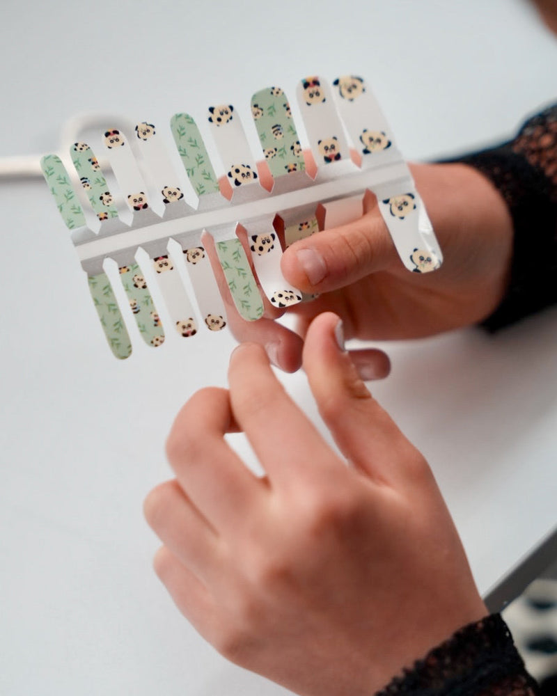 Nahaufnahme einer Kinderhand mit Sheesh Nails Kinder-Nagelfolien „Panda“. Die selbstklebenden Sticker zeigen süße Pandabären und Bambusmotive in Grün und Weiß. Das verspielte Design sorgt für einen freundlichen, kindgerechten Look. Die Folien sind hautfreundlich, ungiftig und leicht anzubringen – ideal für kreative Kinder-Maniküren mit Tiermotiven.