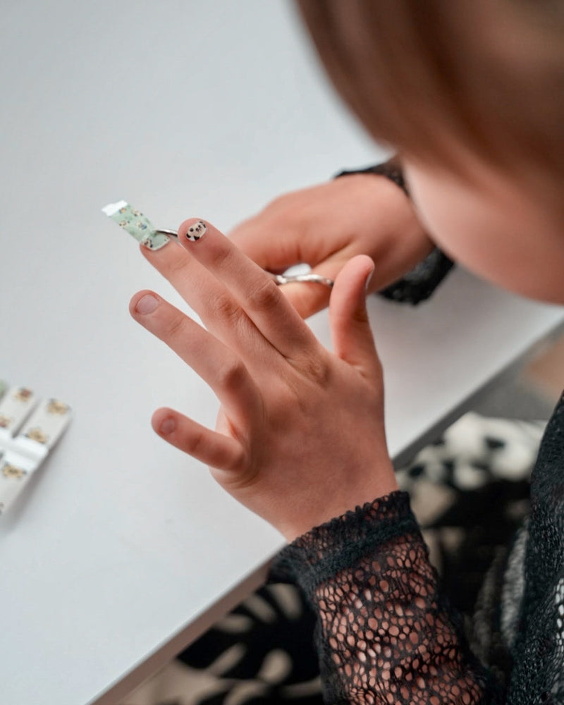 Nahaufnahme einer Kinderhand mit Sheesh Nails Kinder-Nagelfolien „Panda“. Die selbstklebenden Sticker zeigen süße Pandabären und Bambusmotive in Grün und Weiß. Das verspielte Design sorgt für einen freundlichen, kindgerechten Look. Die Folien sind hautfreundlich, ungiftig und leicht anzubringen – ideal für kreative Kinder-Maniküren mit Tiermotiven.