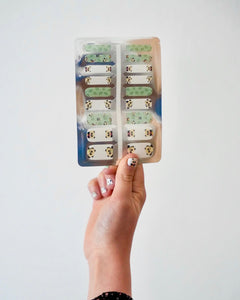 Nahaufnahme einer Kinderhand, die die Sheesh Nails Kinder-Nagelfolien „Panda“ in der Verpackung hält. Die selbstklebenden Sticker zeigen niedliche Pandabären auf grün-weißem Hintergrund mit Bambusdetails. Das verspielte Design sorgt für einen fröhlichen, kindgerechten Look. Die Folien sind hautfreundlich, ungiftig und leicht anzubringen – ideal für kreative Kinder-Maniküren mit Tiermotiven.