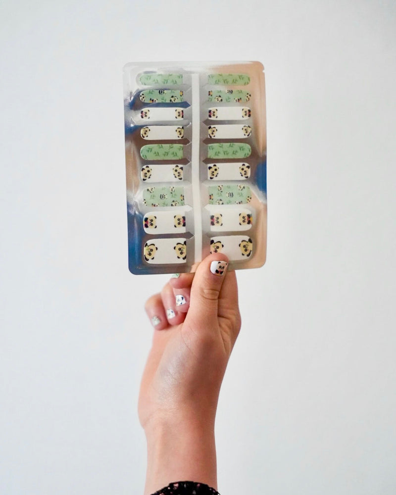 Nahaufnahme einer Kinderhand, die die Sheesh Nails Kinder-Nagelfolien „Panda“ in der Verpackung hält. Die selbstklebenden Sticker zeigen niedliche Pandabären auf grün-weißem Hintergrund mit Bambusdetails. Das verspielte Design sorgt für einen fröhlichen, kindgerechten Look. Die Folien sind hautfreundlich, ungiftig und leicht anzubringen – ideal für kreative Kinder-Maniküren mit Tiermotiven.