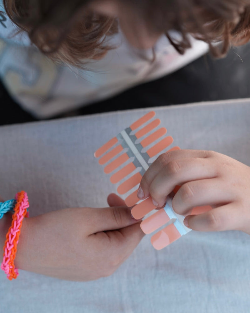 Nahaufnahme einer Kinderhand mit den Sheesh Nails Kinder-Nagelfolien „Peach“. Die zarten Pfirsichfarben verleihen kleinen Nägeln einen weichen, natürlichen Look. Die selbstklebenden, deckenden Sticker lassen sich leicht aufkleben und rückstandsfrei wieder entfernen – ganz ohne UV-Lampe. Das Design wirkt warm, freundlich und sorgt für eine gepflegte Kinder-Maniküre mit sanftem Glanz. Hautfreundlich, ungiftig und perfekt für kreative kleine Nail-Artists.