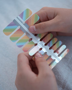 Nahaufnahme einer Kinderhand mit Sheesh Nails Kinder-Nagelfolien „Rainbow“. Die selbstklebenden Sticker zeigen ein fröhliches Regenbogendesign in sanften Pastelltönen. Das deckende Finish sorgt für einen gleichmäßigen, farbintensiven Look. Die Folien sind leicht anzubringen, hautfreundlich, ungiftig und lassen sich rückstandsfrei wieder entfernen – ideal für kreative Kinder-Maniküren mit Farbe und Spaß.