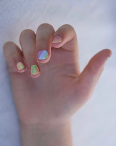 Nahaufnahme einer Kinderhand mit Sheesh Nails Kinder-Nagelfolien „Rainbow“. Die selbstklebenden Sticker zeigen ein fröhliches Regenbogendesign in sanften Pastelltönen. Das deckende Finish sorgt für einen gleichmäßigen, farbintensiven Look. Die Folien sind leicht anzubringen, hautfreundlich, ungiftig und lassen sich rückstandsfrei wieder entfernen – ideal für kreative Kinder-Maniküren mit Farbe und Spaß.
