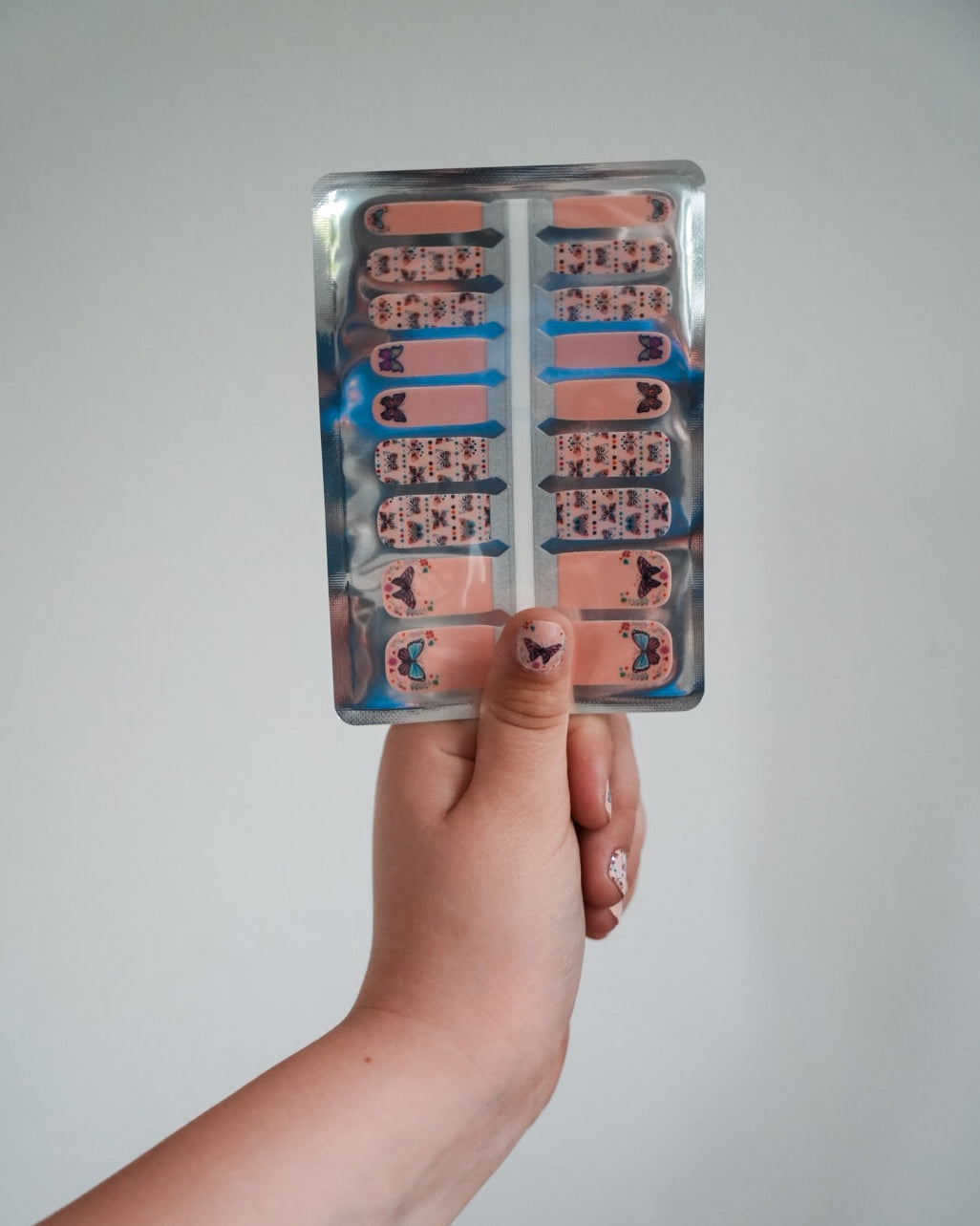 Nahaufnahme einer Kinderhand mit den Sheesh Nails Kinder-Nagelfolien „Schmetterling“. Die selbstklebenden Sticker zeigen ein verspieltes Design mit bunten Schmetterlingen auf rosafarbenem Hintergrund. Das deckende Finish sorgt für einen fröhlichen, kindgerechten Look. Hautfreundlich, ungiftig und leicht anzubringen – ideal für kreative Kinder-Maniküren voller Farbe und Fantasie.