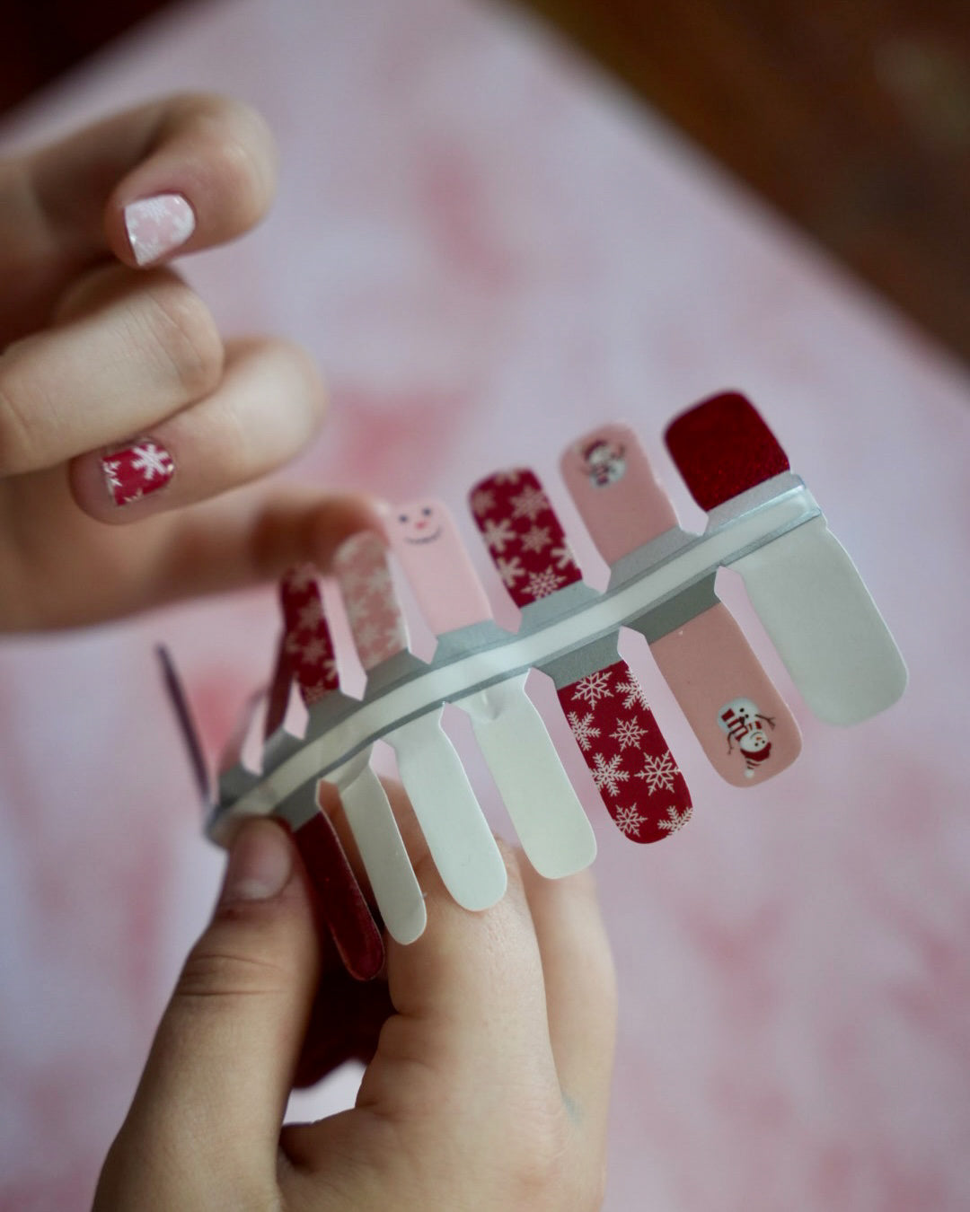Kinderhand appliziert rote und rosafarbene Kinder-Nagelfolien mit Schneemann- und Schneeflocken-Motiv von SHEESH Nails – weihnachtliches Winter Nail Design für Kinderhände.

