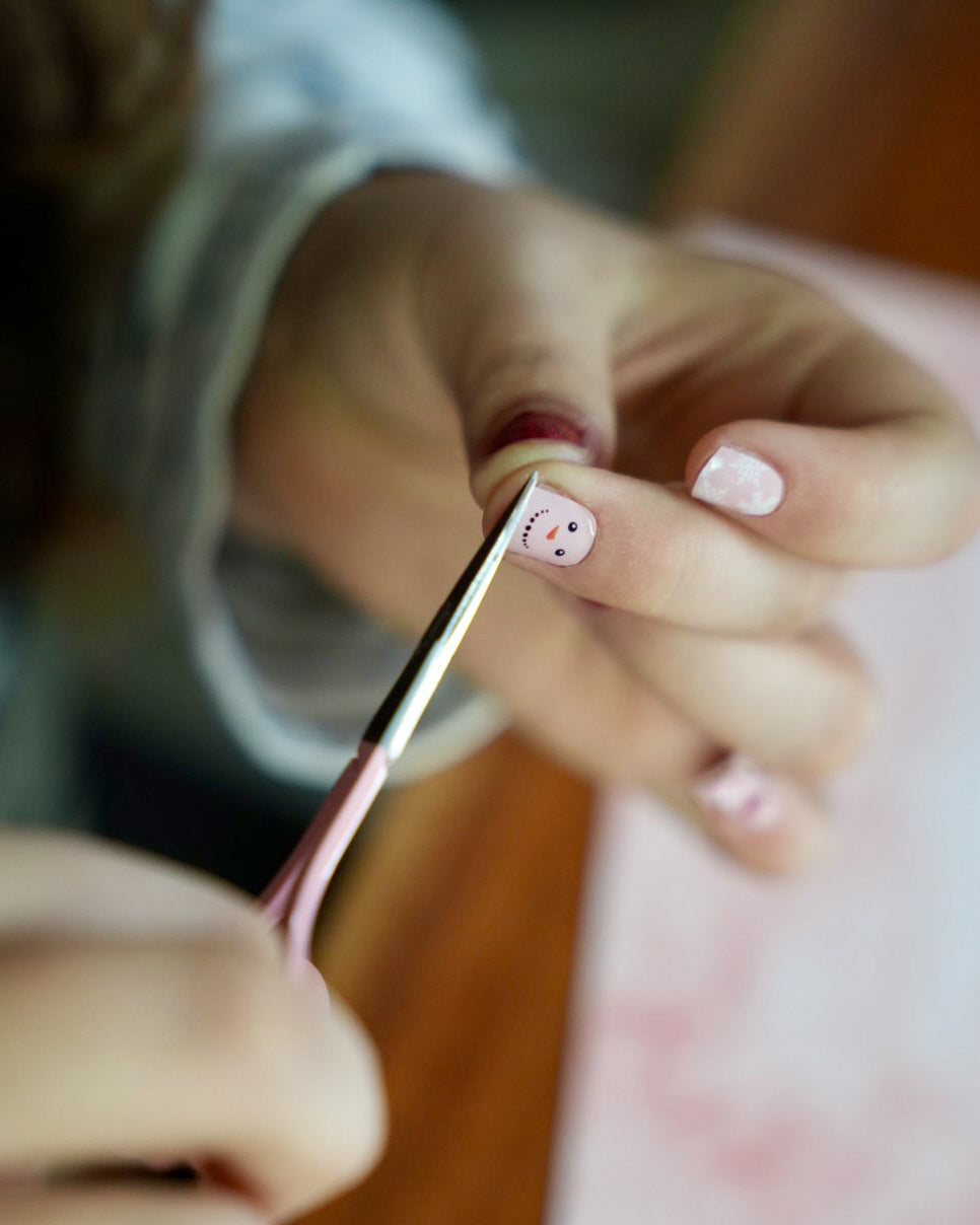 Kinderhand schneidet die rote und rosafarbene Kinder-Nagelfolien mit Schneemann- und Schneeflocken-Motiv am Nagel ab. Sie ist von SHEESH Nails – weihnachtliches Winter Nail Design für Kinderhände.