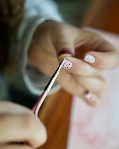 Kinderhand schneidet die rote und rosafarbene Kinder-Nagelfolien mit Schneemann- und Schneeflocken-Motiv am Nagel ab. Sie ist von SHEESH Nails – weihnachtliches Winter Nail Design für Kinderhände.