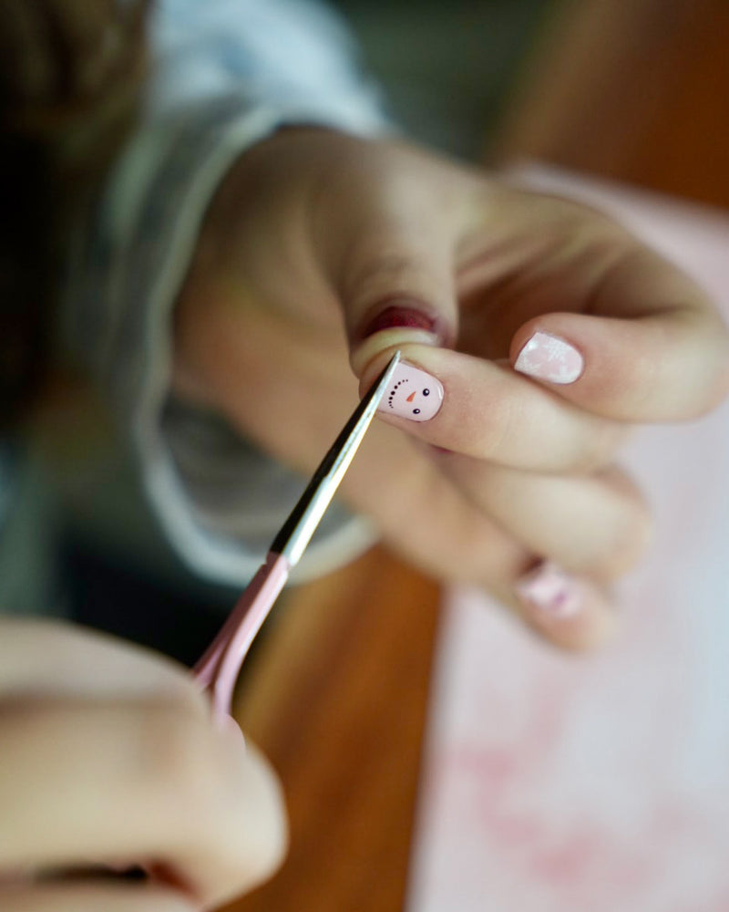 Kinderhand schneidet die rote und rosafarbene Kinder-Nagelfolien mit Schneemann- und Schneeflocken-Motiv am Nagel ab. Sie ist von SHEESH Nails – weihnachtliches Winter Nail Design für Kinderhände.