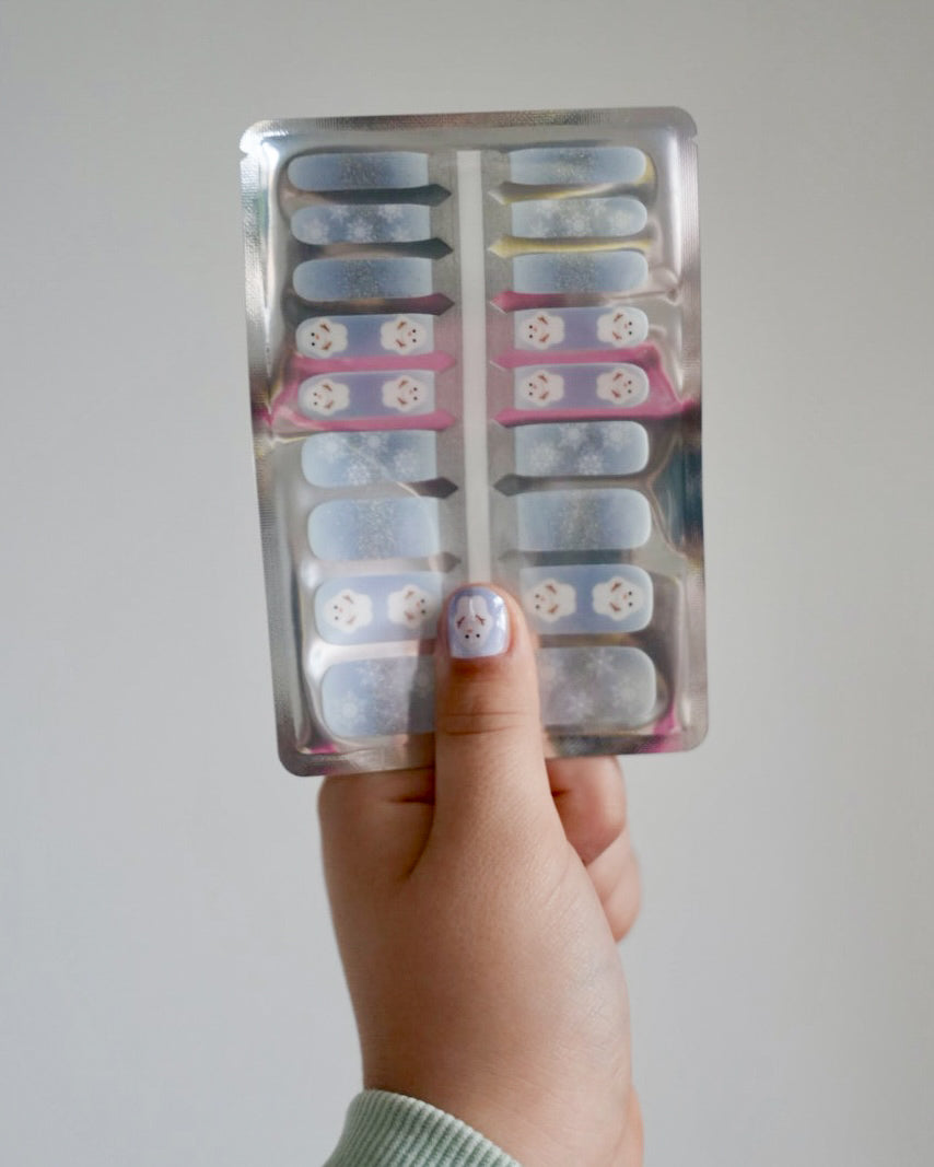 Kinderhand hältt blaue Schneemann Nagelfolien von SHEESH vor weißem Hintergrund  - winterliches Nageldesign für Kinder mit Schneemann-Motiv. 