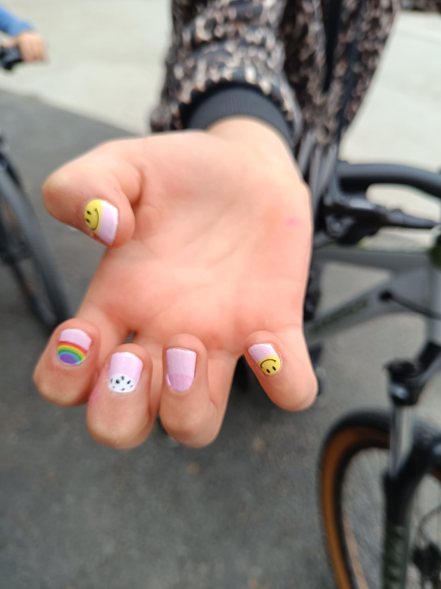 Nahaufnahme eines Kindes mit Sheesh Nails Kinder-Nagelfolien „Smiley“. Die selbstklebenden Sticker zeigen ein buntes, fröhliches Design mit kleinen Smileys und Pastellfarben. Das deckende Finish sorgt für einen lebhaften Look, der Spaß und Kreativität ausdrückt. Die Folien sind leicht anzubringen, hautfreundlich, ungiftig und lassen sich rückstandsfrei wieder entfernen – ideal für farbenfrohe Kinder-Maniküren.