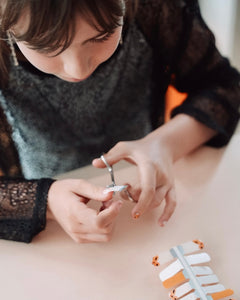 Nahaufnahme einer Kinderhand mit Sheesh Nails Kinder-Nagelfolien „Sonnenblume“. Die selbstklebenden Sticker zeigen ein fröhliches Design mit orangefarbenen und weißen Streifen sowie kleinen Sonnenblumenmotiven. Das verspielte Muster sorgt für einen sommerlichen, kindgerechten Look. Die Folien sind hautfreundlich, ungiftig und leicht anzubringen – ideal für kreative Kinder-Maniküren mit Blumenmotiven.