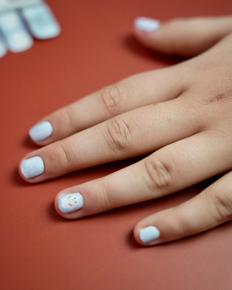 Kinderhand mit blaue Schneemann Nagelfolien von SHEESH auf rotem Hintergrund  winterliches Nageldesign für Kinder mit Schneemann-Motiv. 