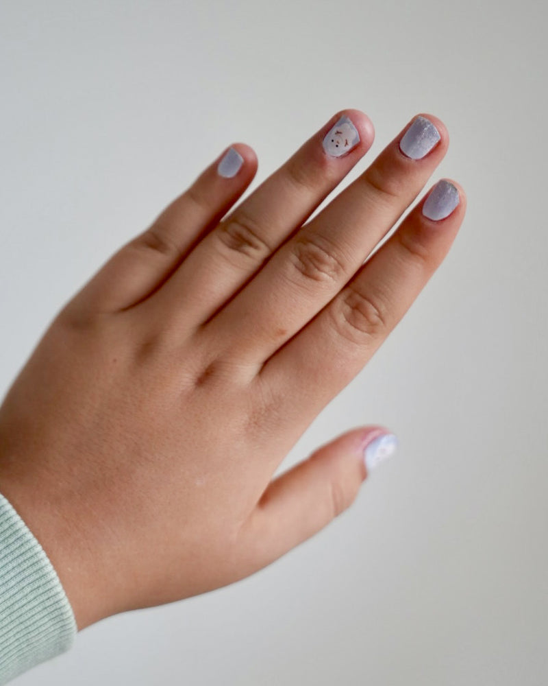 Kinderhand mit blaue Schneemann Nagelfolien von SHEESH vor weißem Hintergrund  - winterliches Nageldesign für Kinder mit Schneemann-Motiv. 
