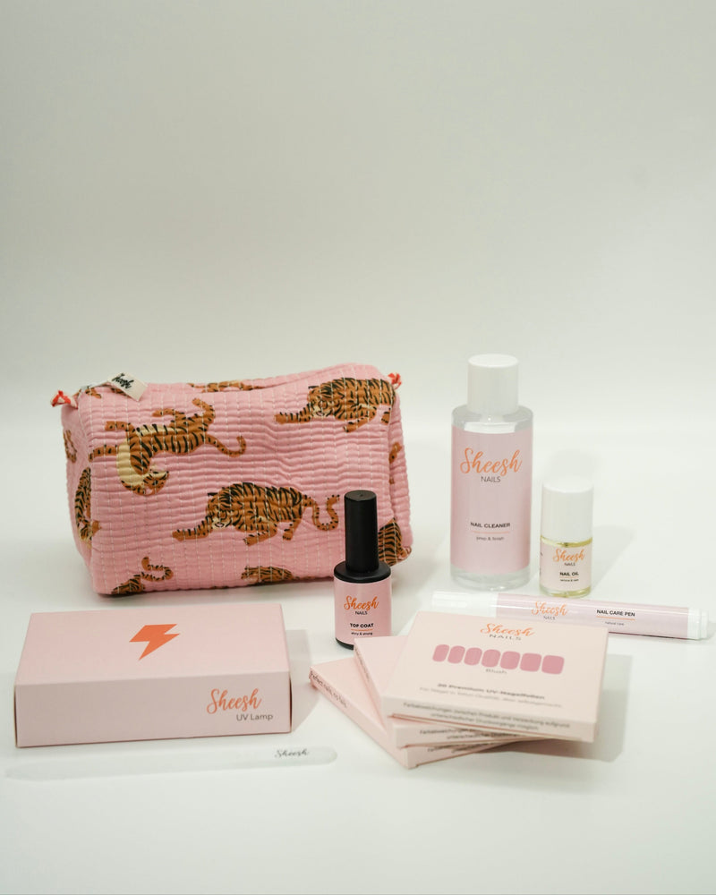 Produktfoto des Sheesh Nails Limited Wild Starter Sets. Eine rosa Kosmetiktasche mit Tigerprint ist gefüllt mit Sheesh Nails Produkten wie UV-Lampe, Nail Care Pen, Cleaner und Nagelfolien. Das Set kombiniert Funktionalität mit stilvollem Design – ideal als Geschenk oder Einstieg in die Nagelfolienwelt.